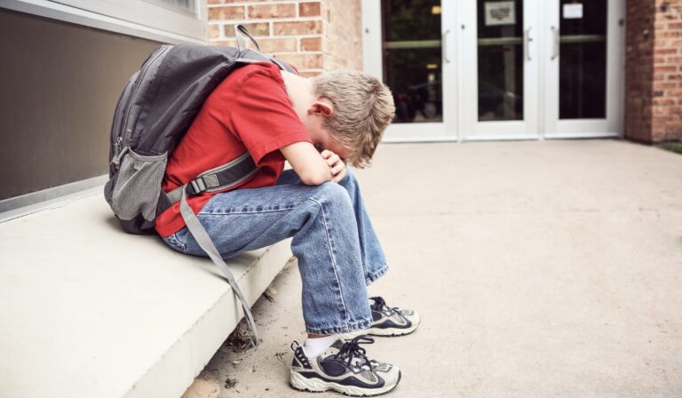 child sitting on bench with head on his arms