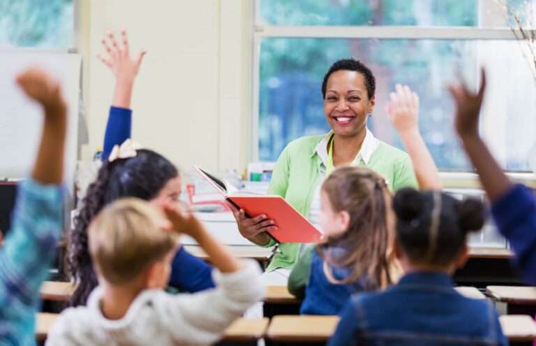 smiling teacher reading to students with their hands in the air