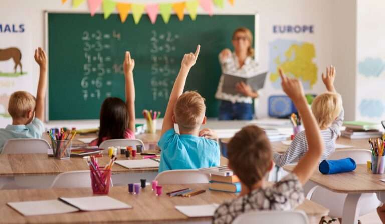 students in classroom with hands in the air