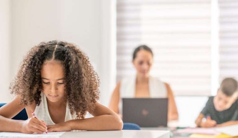 student working independently while classroom paraprofessional observes from the back of the inclusive classroom
