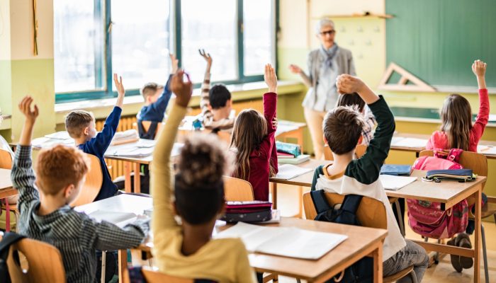 class of elementary students raising their hands