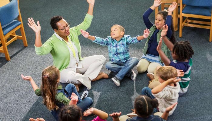 teacher and students sitting on floor in a circle with arms in the air for a brain break