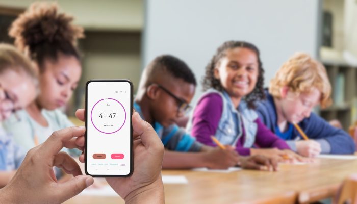 hand holding a phone with a timer on it in a classroom of elementary children