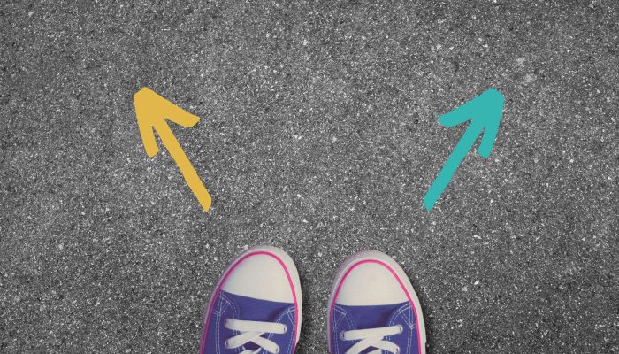 student feet standing on concrete with two arrows pointing different directions, indicating a choice to be made