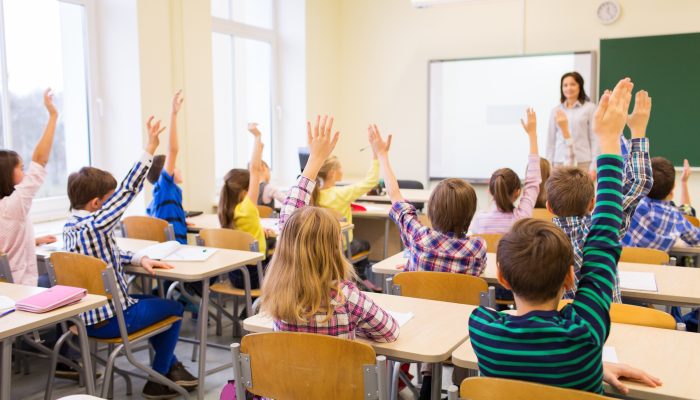 students raising hands to answer teacher's question