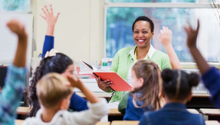 smiling teacher reading to students with their hands in the air